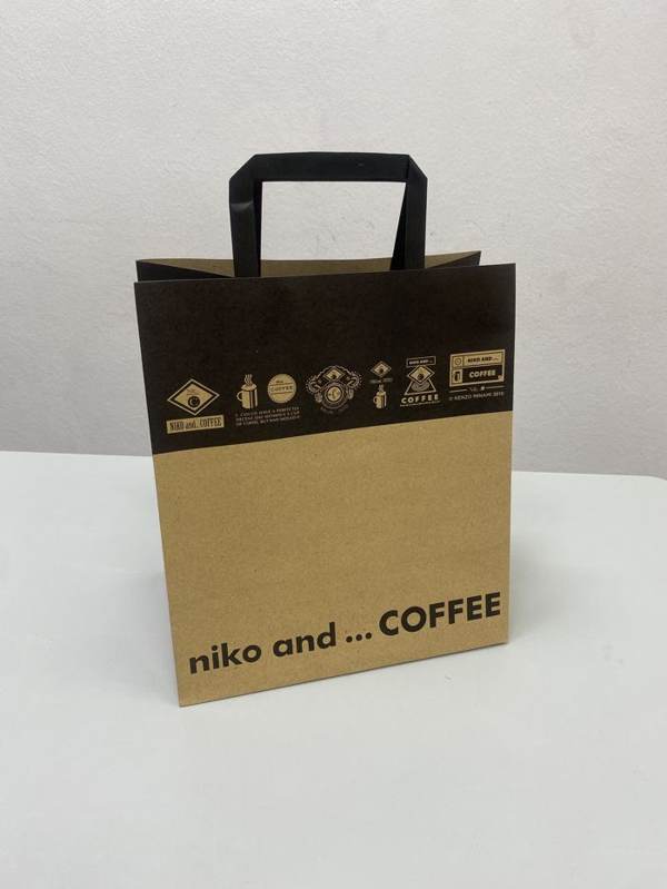 コーヒーブランド「niko and... COFFEE」のクラフト紙製ショップバッグ。黒い持ち手とアイコンイラストが特徴的なデザイン。